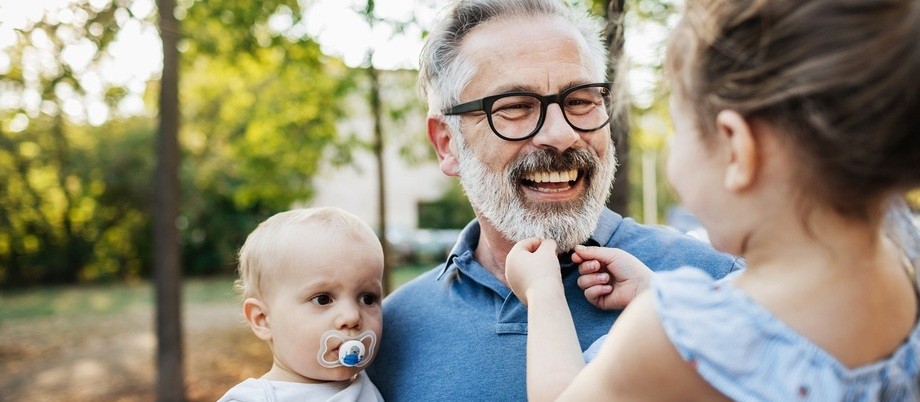Finanzielle Absicherung im Alter: Älterer lachender Mann, der zwei Kinder auf dem Arm hält