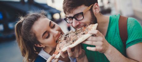 Ein junges Paar ist in der Stadt unterwegs und beißt in ein Pizza-Stück.