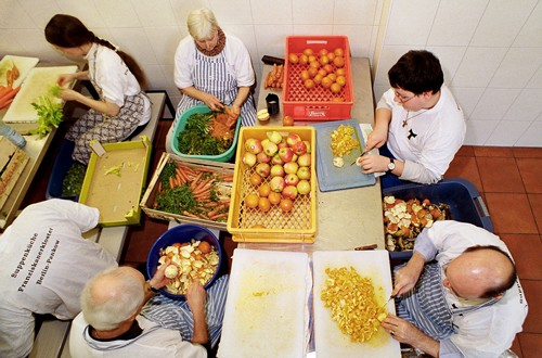 Ältere Menschen schneiden gemeinsam in einer Großküche Gemüse