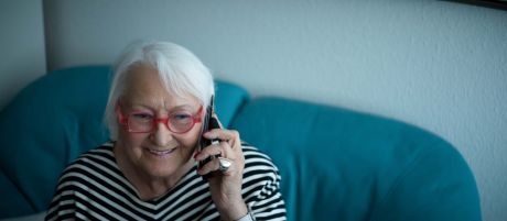 Eine alte Frau hält ein Telefon am Ohr und lächelt.