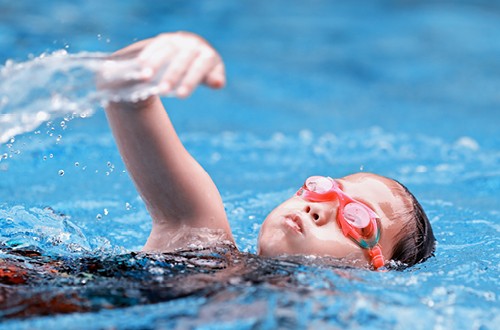 Ein junges Mädchen mit Schwimmbrille krault durch das Wasser.
