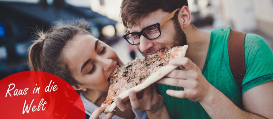 Junges Paar ist in der Stadt unterwegs und beißt in ein Pizza-Stück